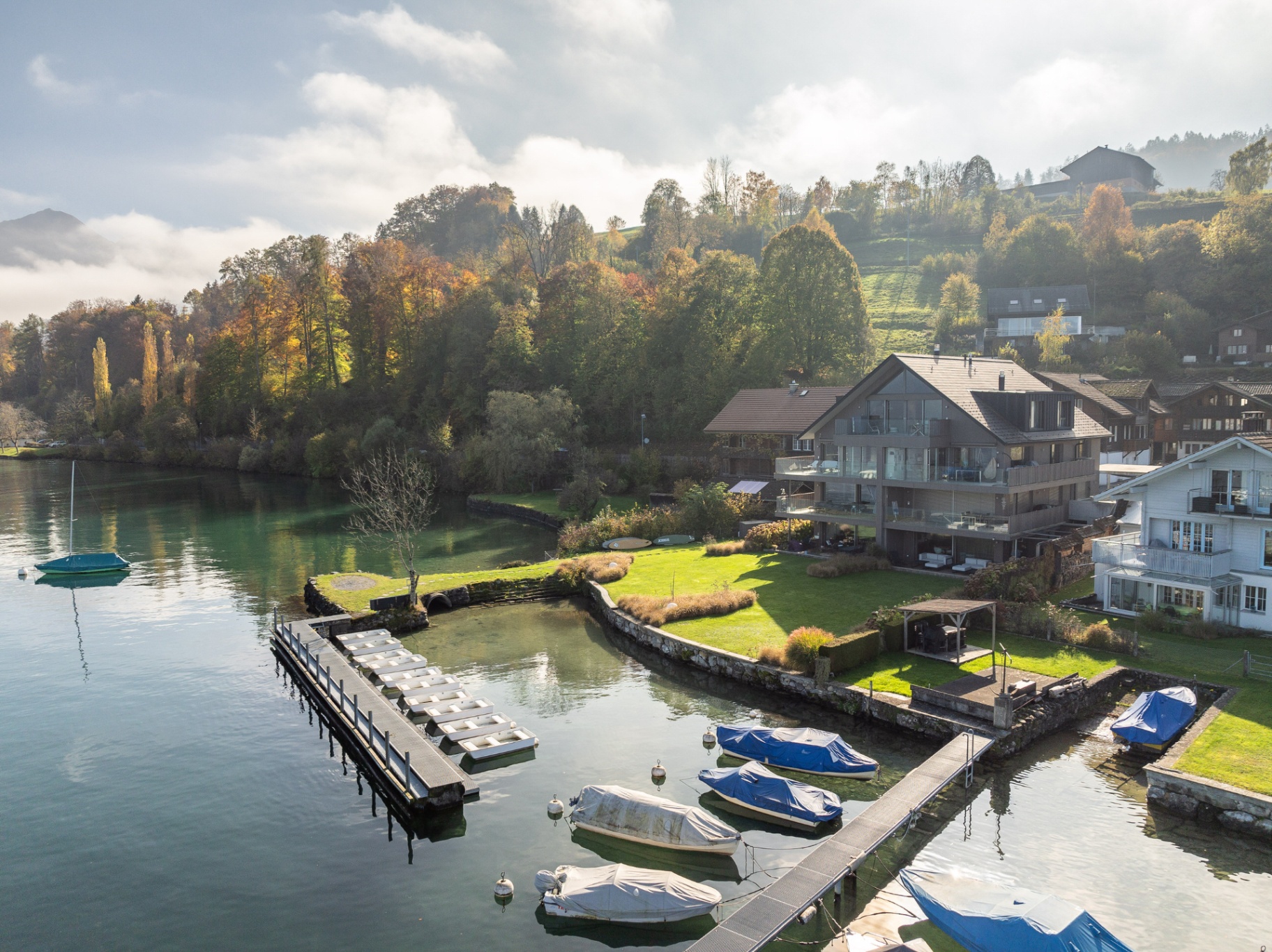 Drohnenaufnahme einer AlpineLake-Ferienwohnung am See im Berner Oberland mit Garten, Booten, Bergen und Umgebung