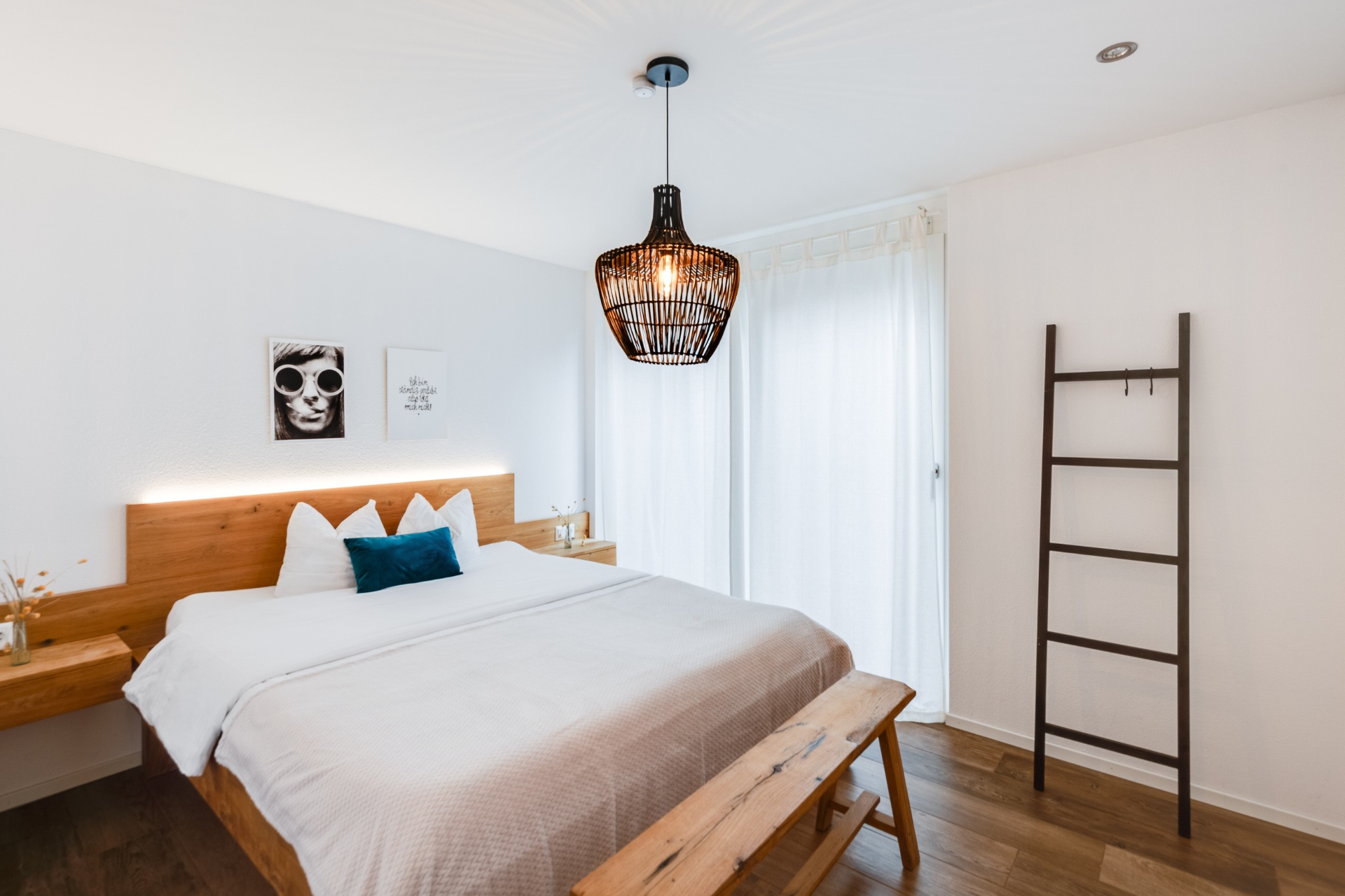 Helles Schlafzimmer einer AlpineLake-Ferienwohnung mit Bett, Holzdetails, Pendelleuchte und ruhiger Atmosphäre